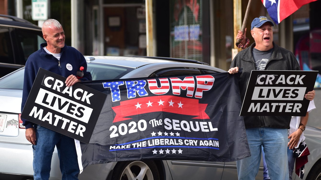 Two men holding a flag that says Trump 2020 The Sequel and banners saying "crack lives matter"
