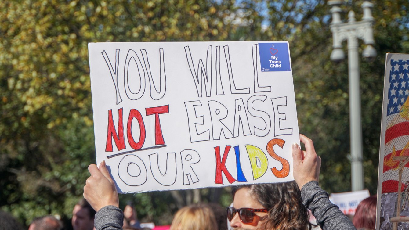 Hands holding up sign reading "You will not erase our kids"