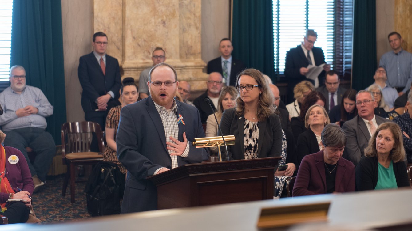 Man standing next to a woman at a podium speaking into microphone