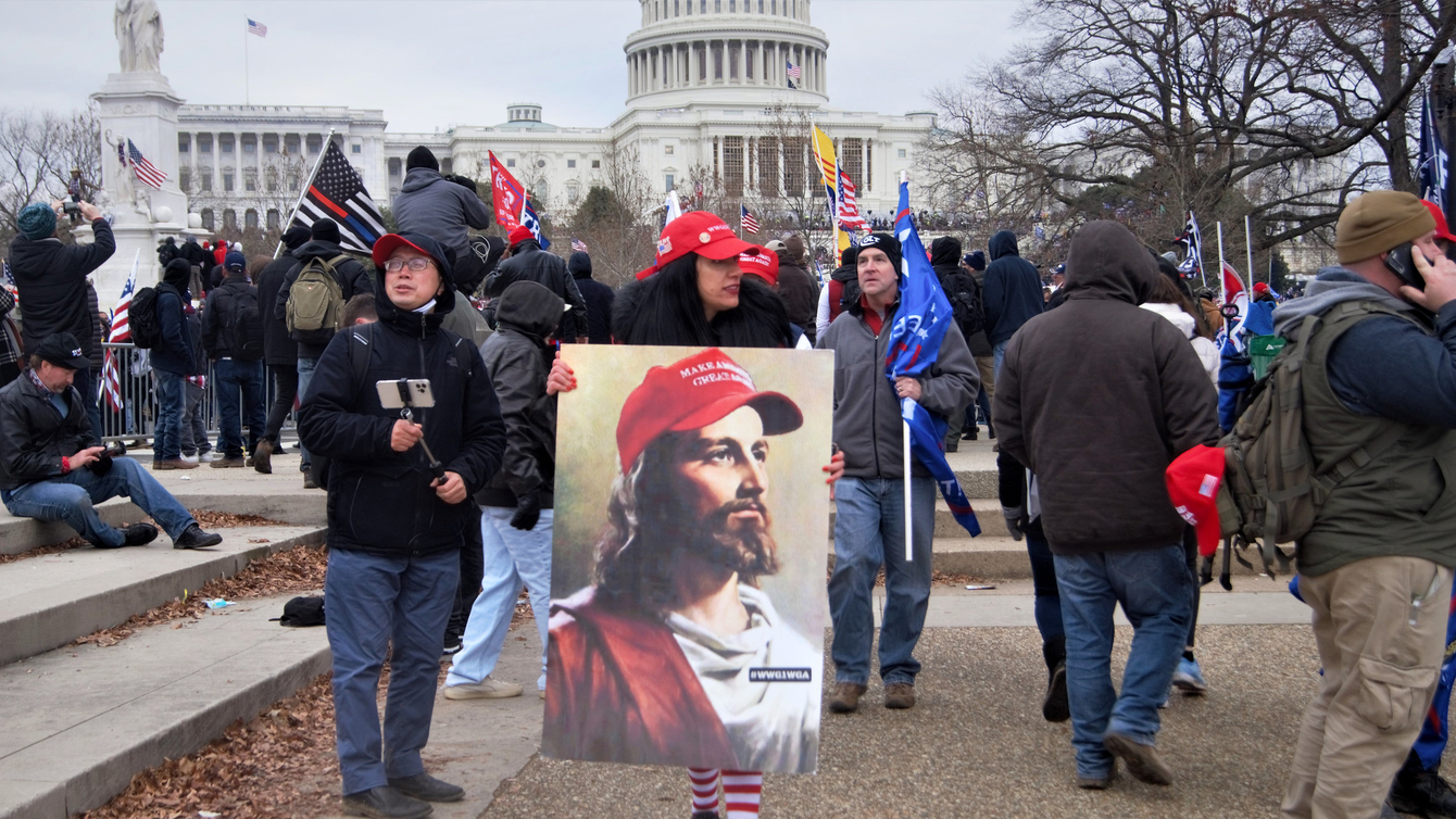 A woman wearing a red hat, holding a paining of Jesus wearing a Make America Great Again hat.