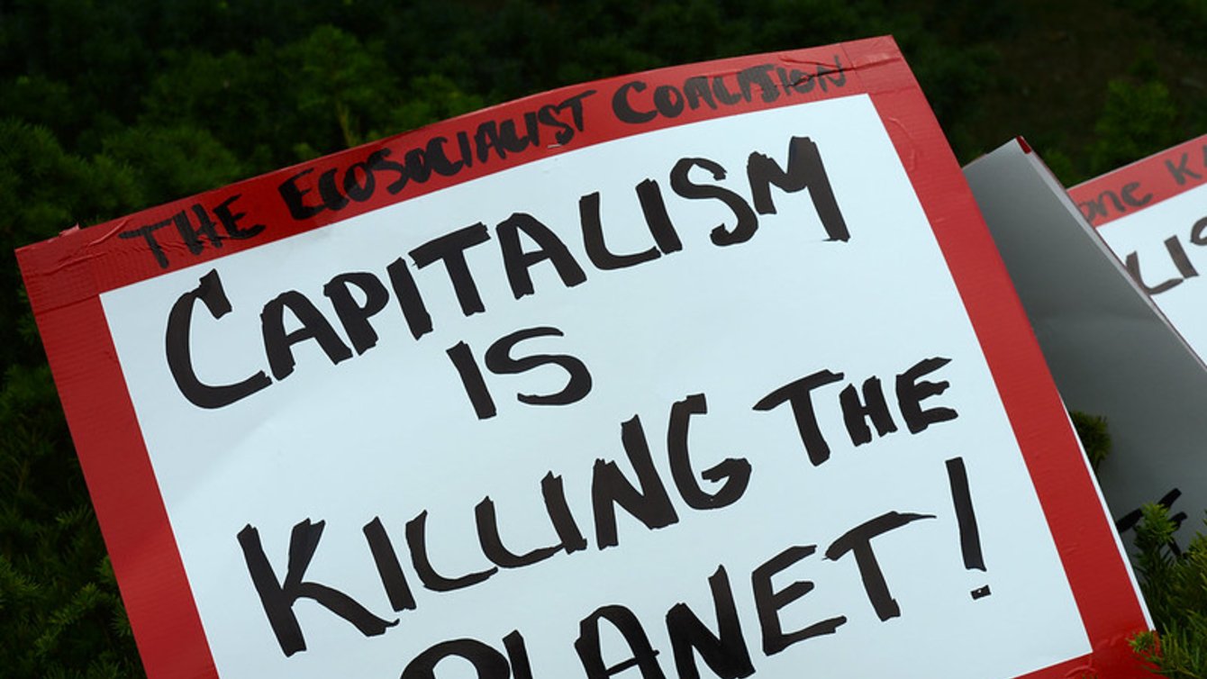 A red and white sign that says "capitalism is killing the planet!"