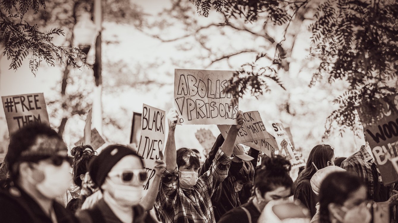 A person at a protest holding a board that says "Abolish Prisons"