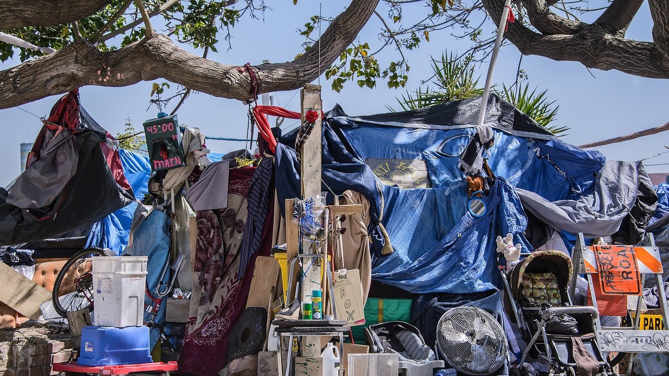 Boxes, prams, tarps, and other disparate items piled up under a blue sky on the sidewalk