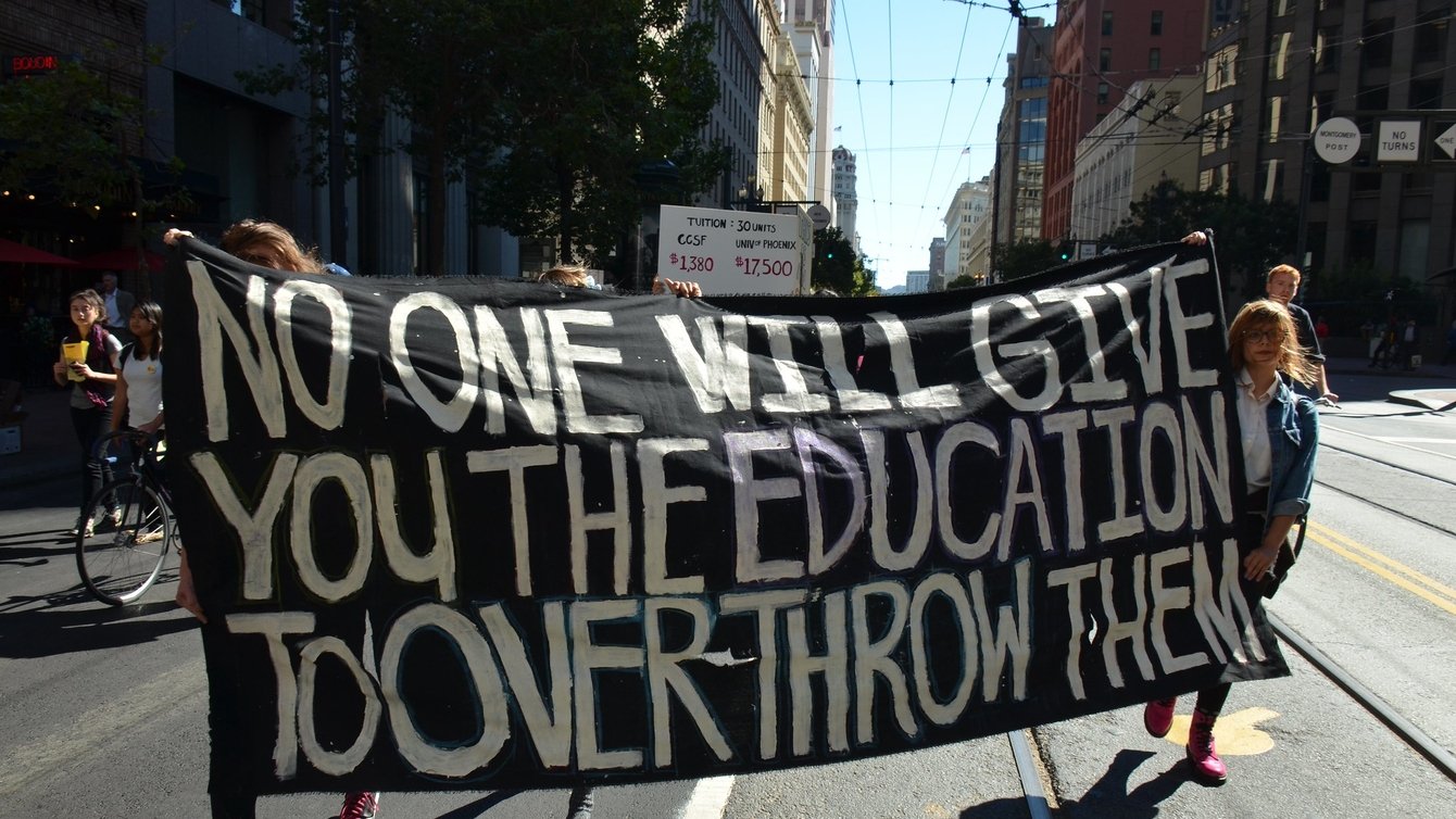 Protesters holding a banner that reads: No one will give you the education to overthrow them