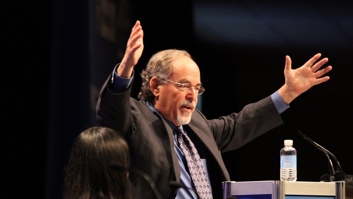 David Horowitz, a white man with his hands raised in the air, in front of a mic stand.