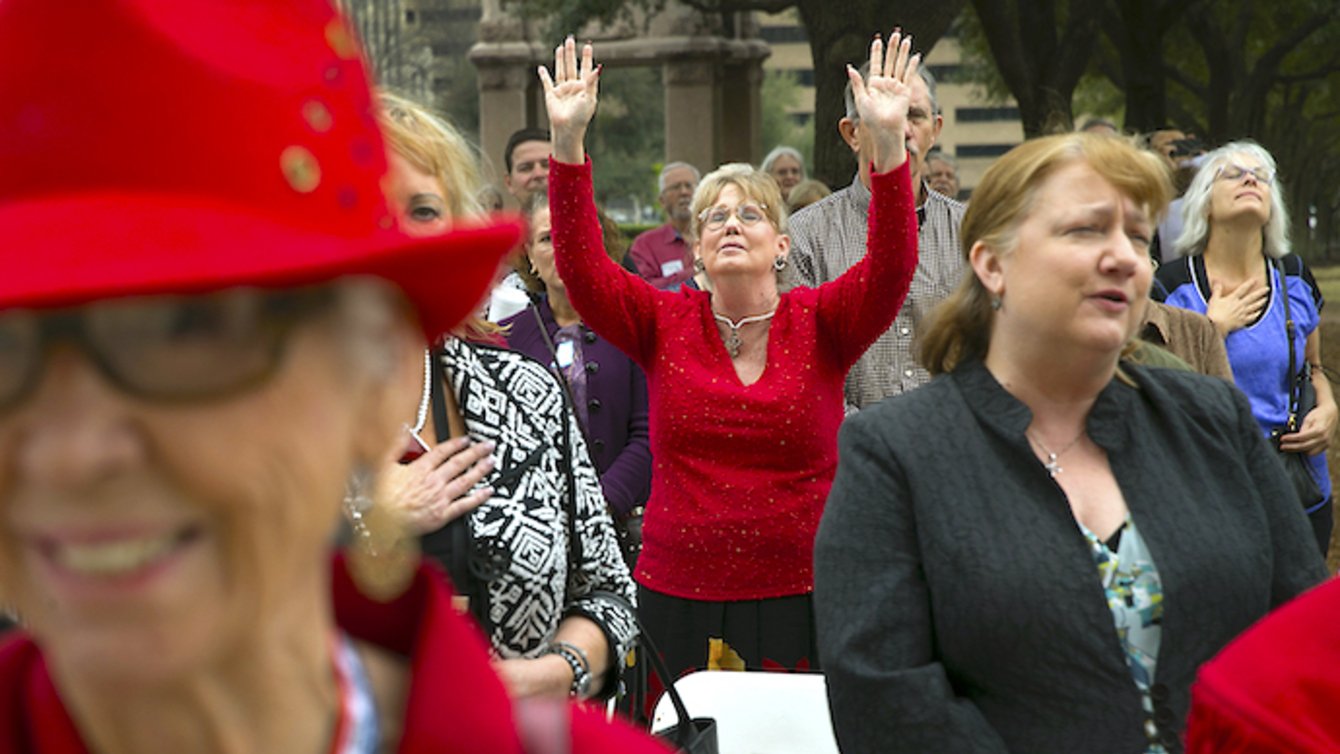 Older woman standing in crowd with both hands raised