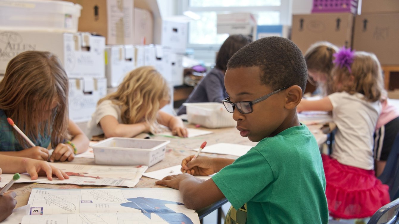 A young boy with glasses in a school, looking at a book.
