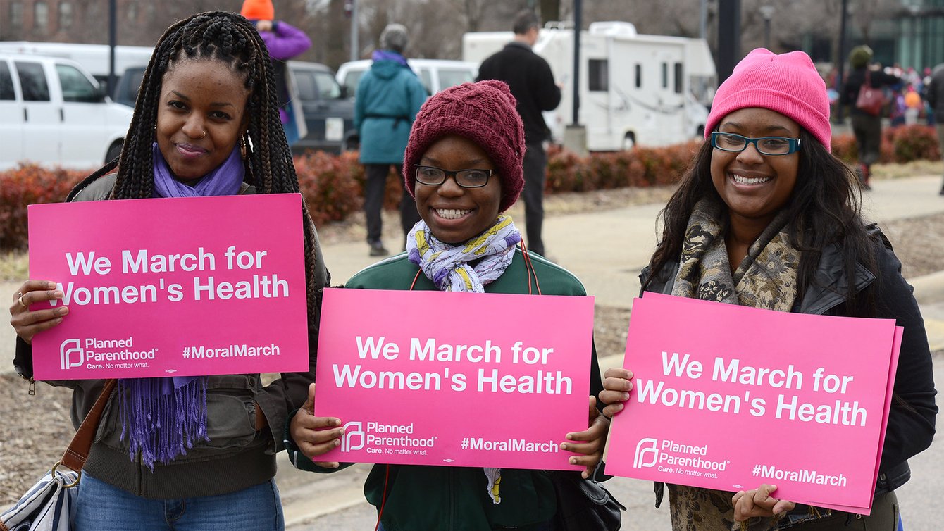 Three women holding signs that say "We march for Woomen's Health."