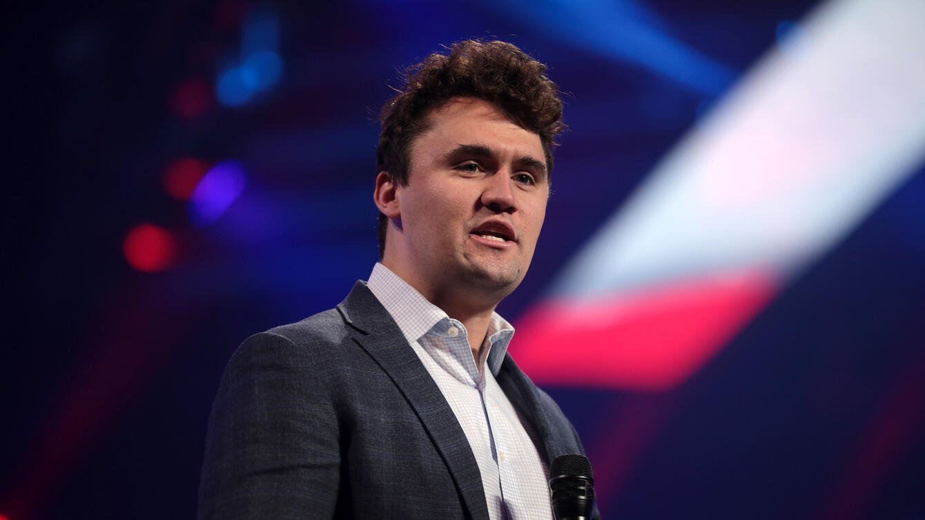 A young white man, Charlie kirk, in a suit, holding a mic.