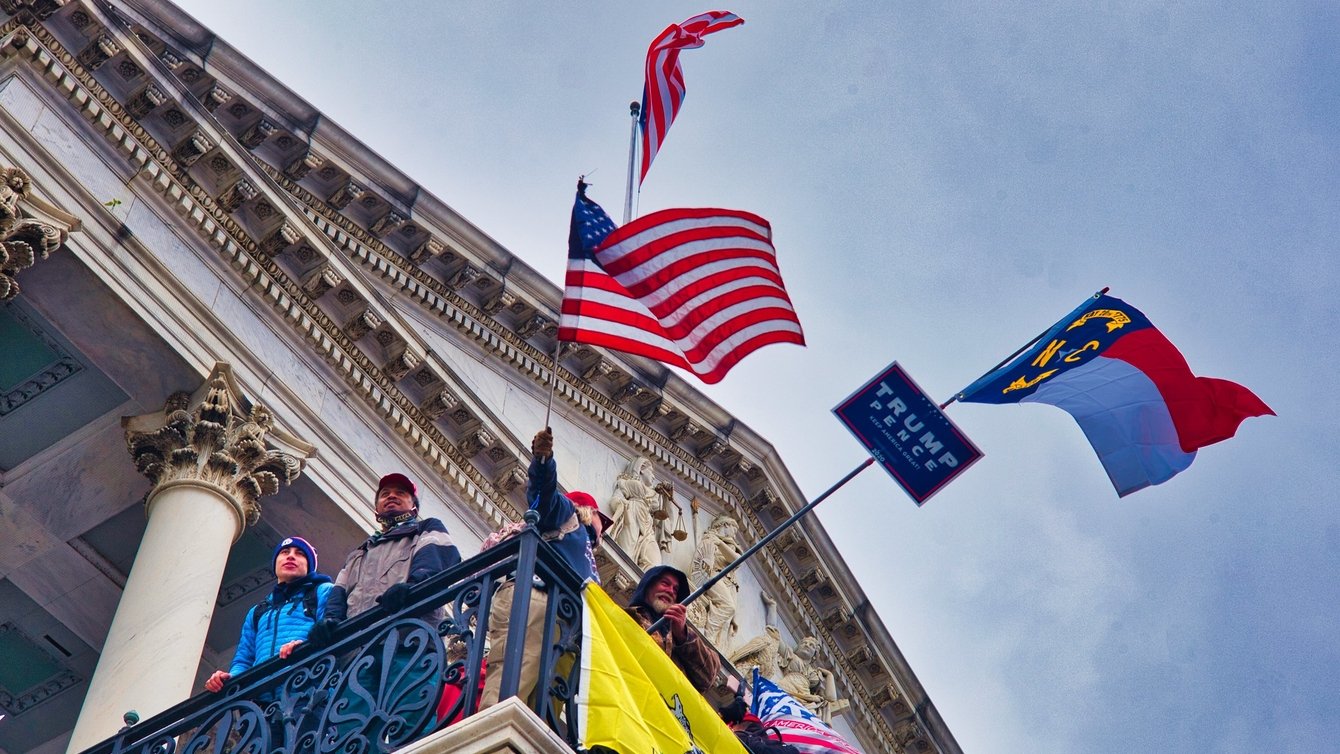 A U.S Flag, A Trump and Pence flag and other flags flying from the balcony of the Capitol building.