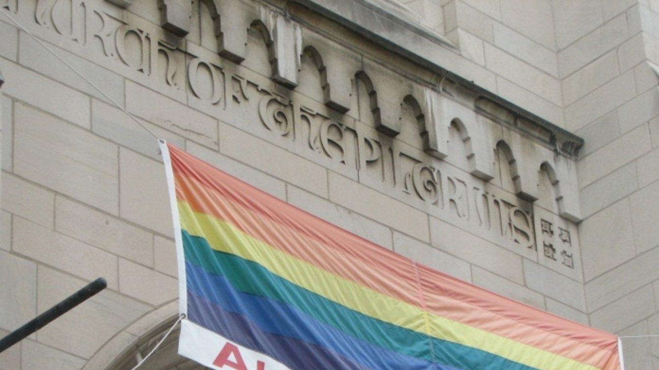 A rainbow flag outside a church with the words "All are welcome"
