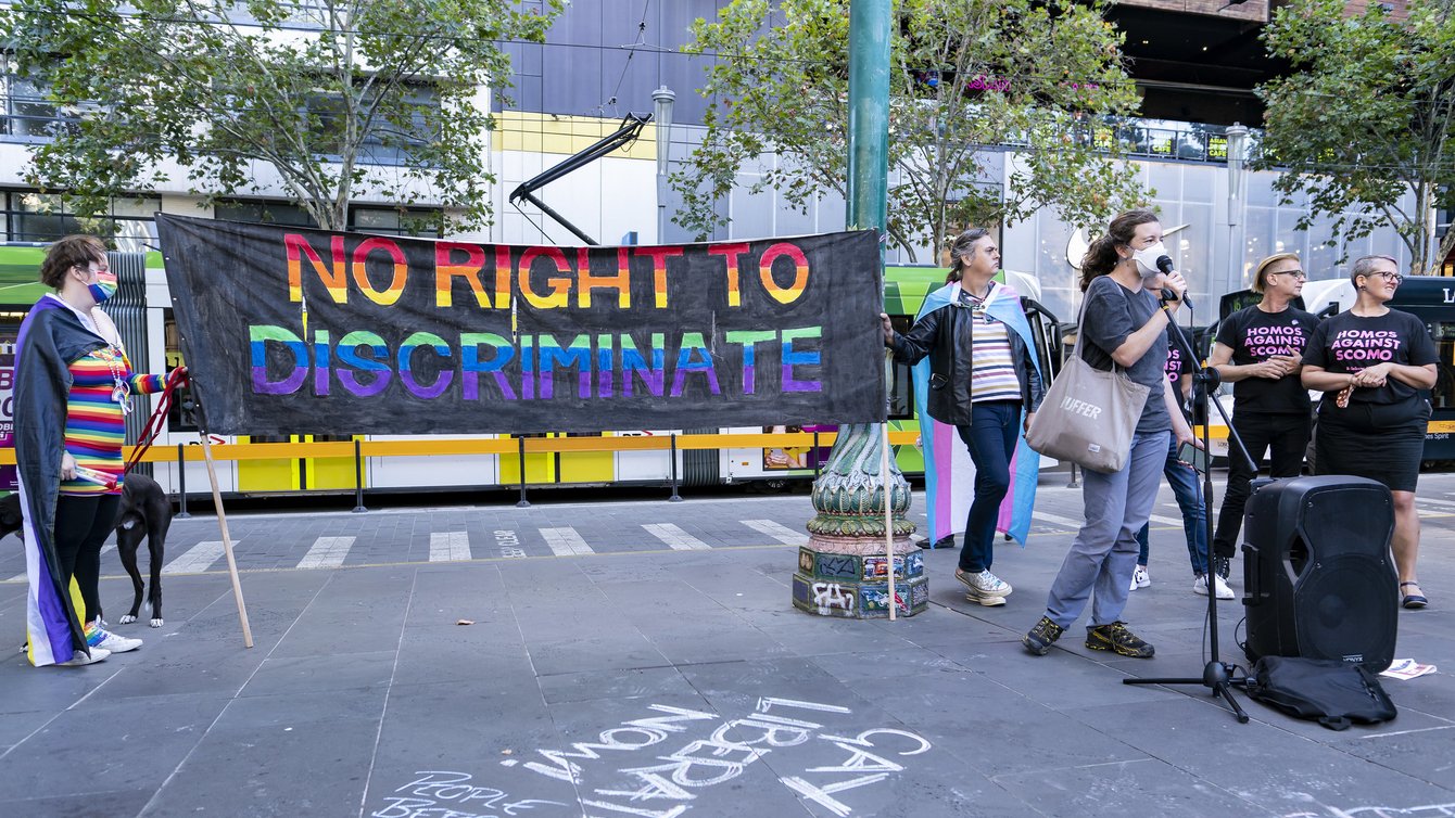Protesters standing around a mic, two people holding a banner that reads "no right to discriminate"