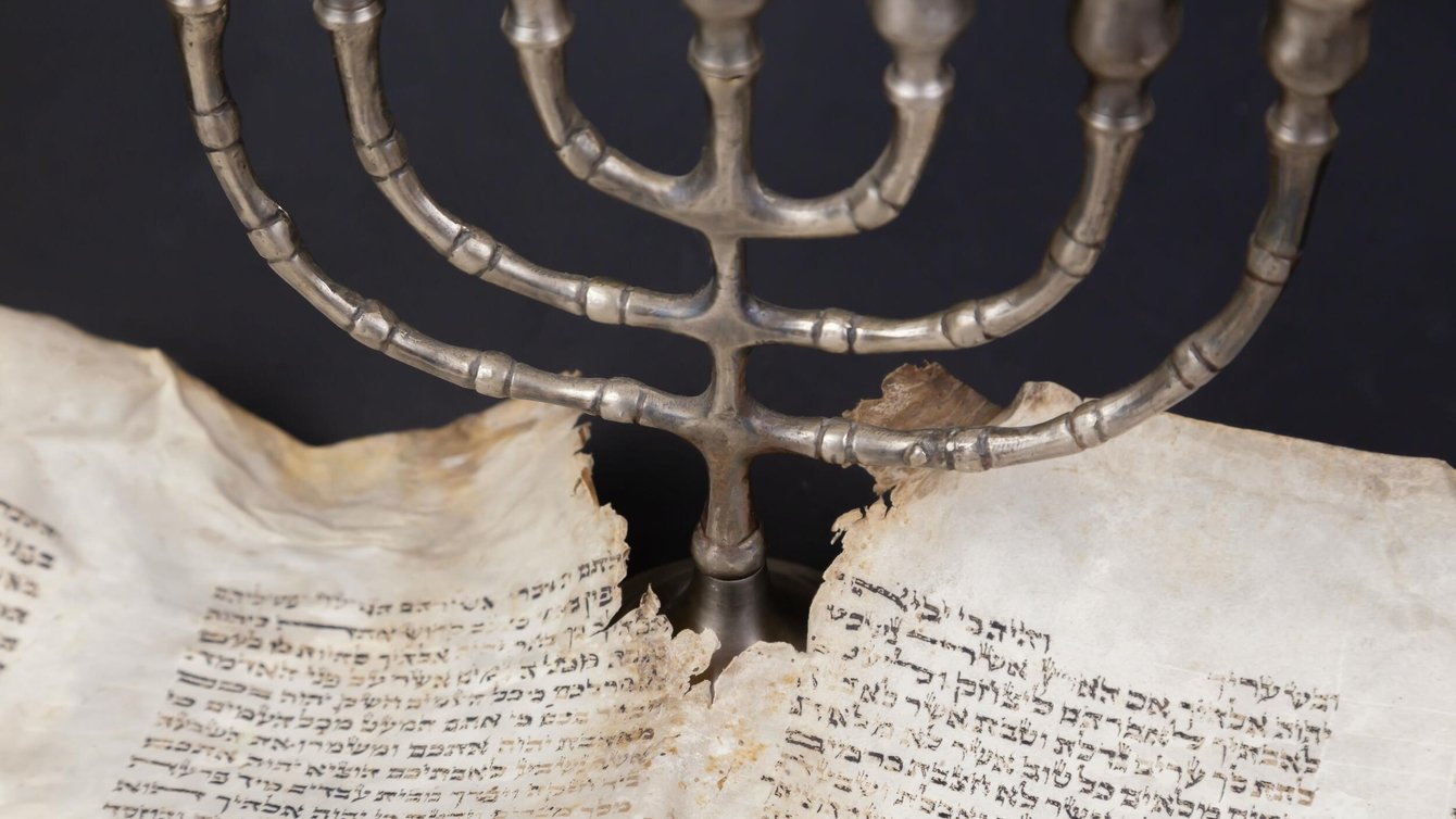 Old scrolls of the Bible and Menorah lie on a black background.