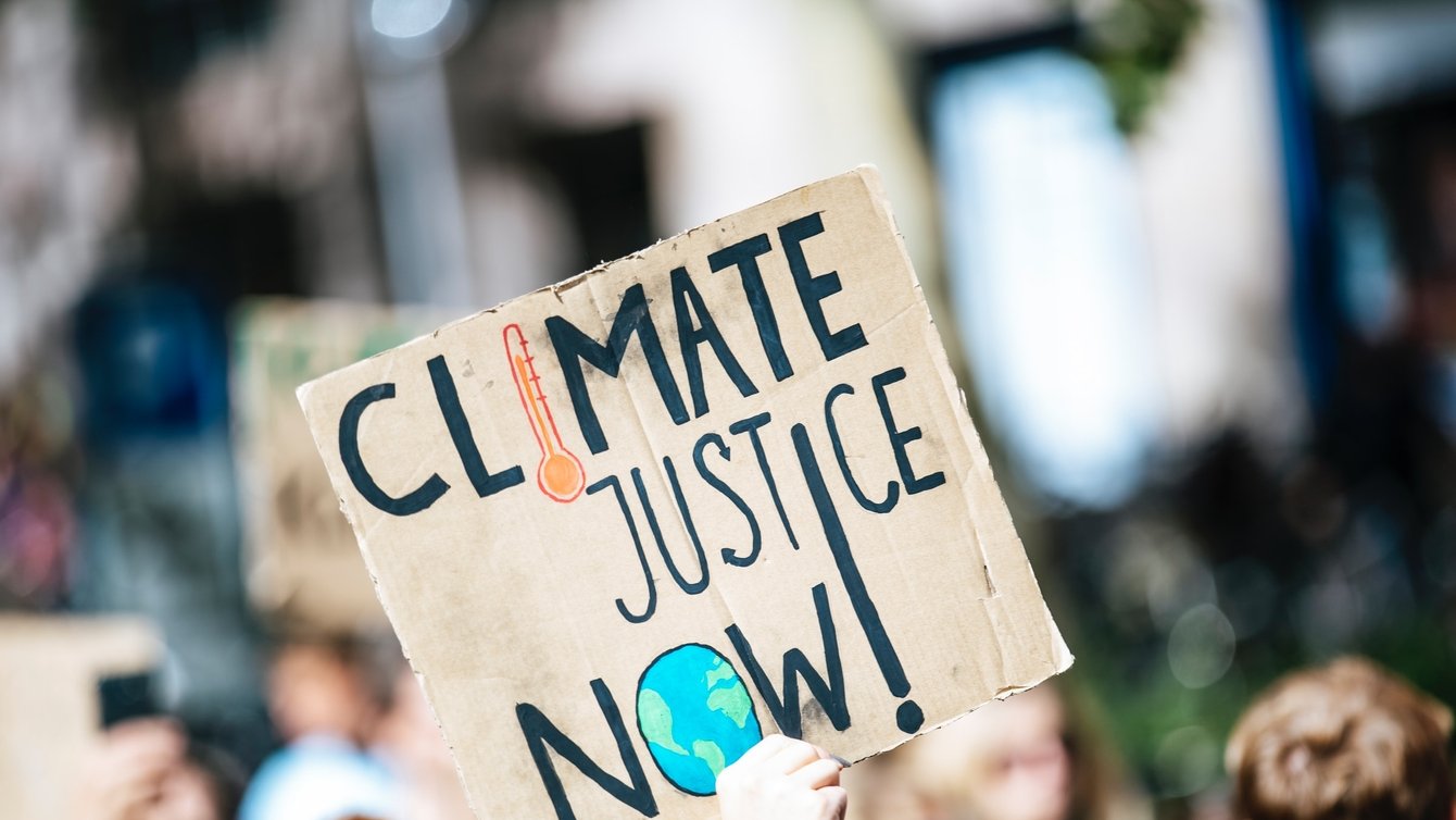 A protestor's hand holding a sign that says, "Climate Justice Now!"