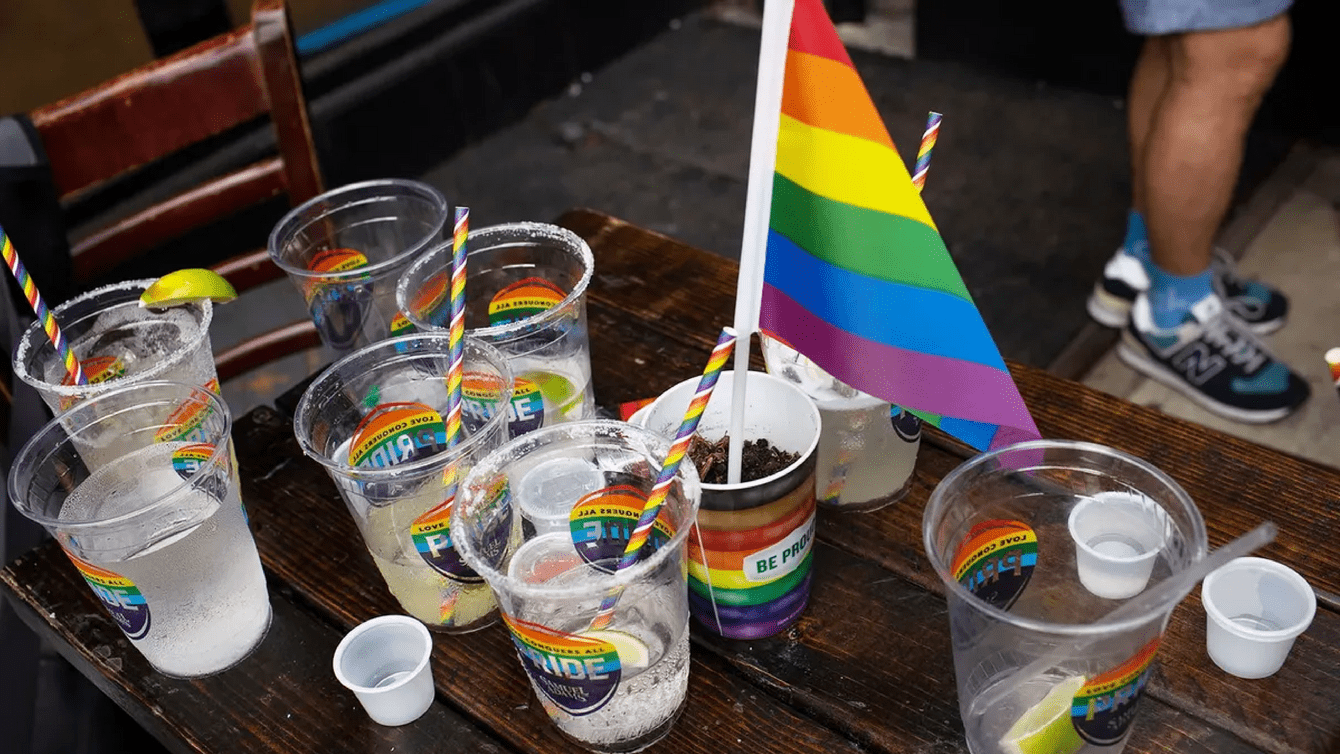 A table with plastic cups that have stickers on them that say "Pride." One of the cups has a rainbow flag in it.