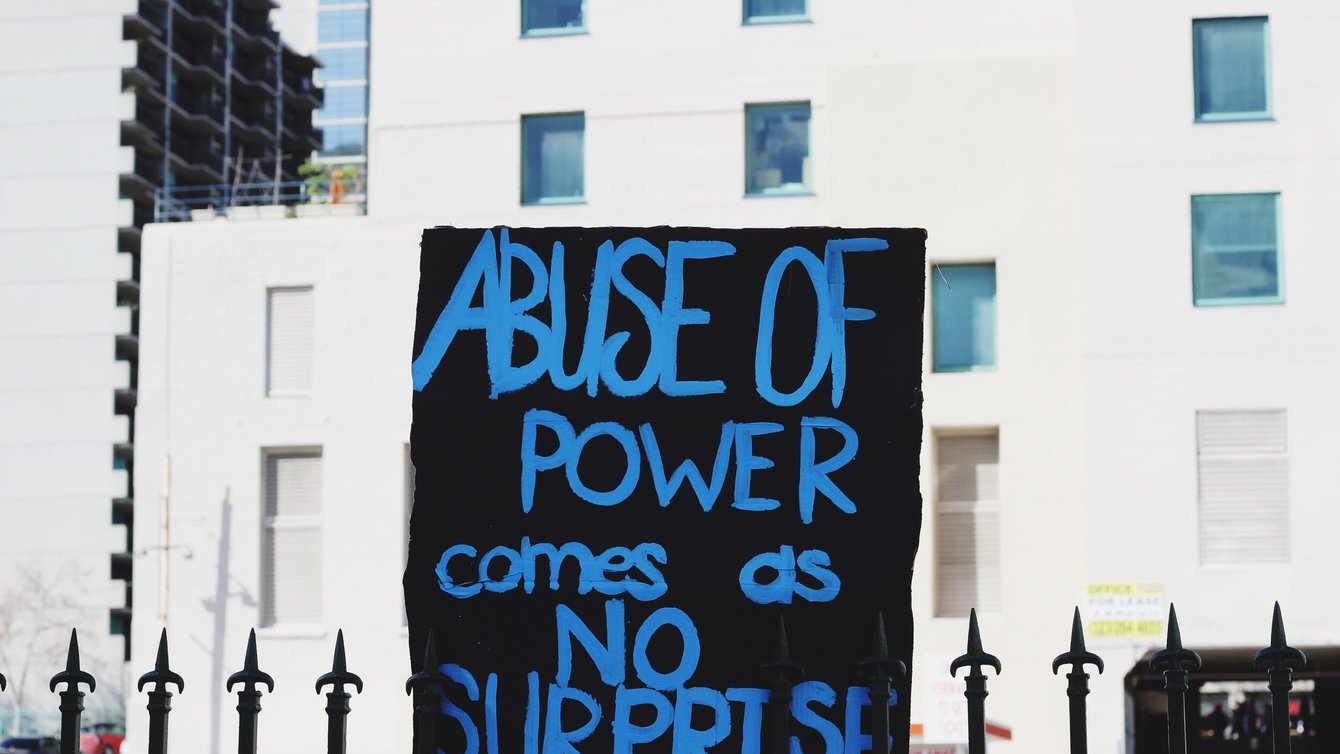 A black sign that says "Abuse of power comes as no surprise."