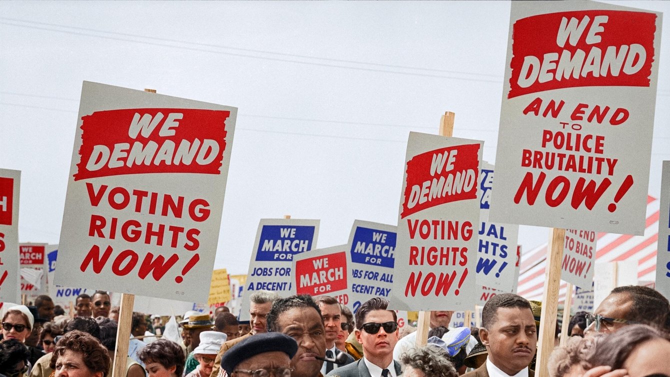 People at a protest holding a sign that says "We Demand Voting rights now!" "We demand An end to police brutality now"
