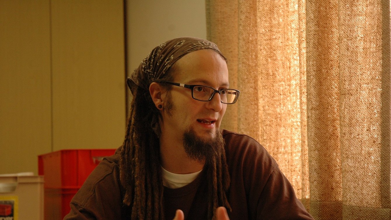 A White man wearing a sweater, with glasses and a bandana and dreadlocks.