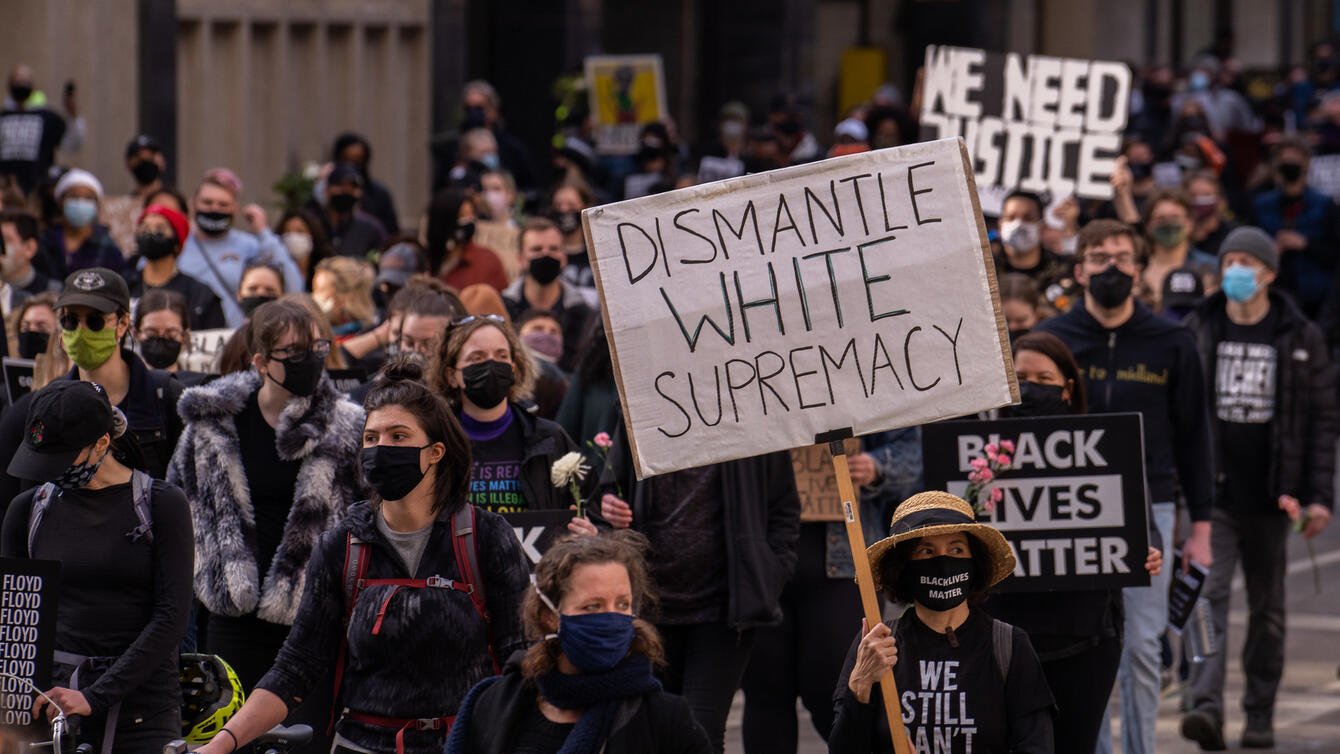 Protestors walking the street, one protestor holding a sign that says "Dismantle White Supremacy."