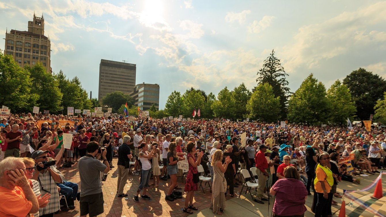 Protesters in a park with buildings in the background.