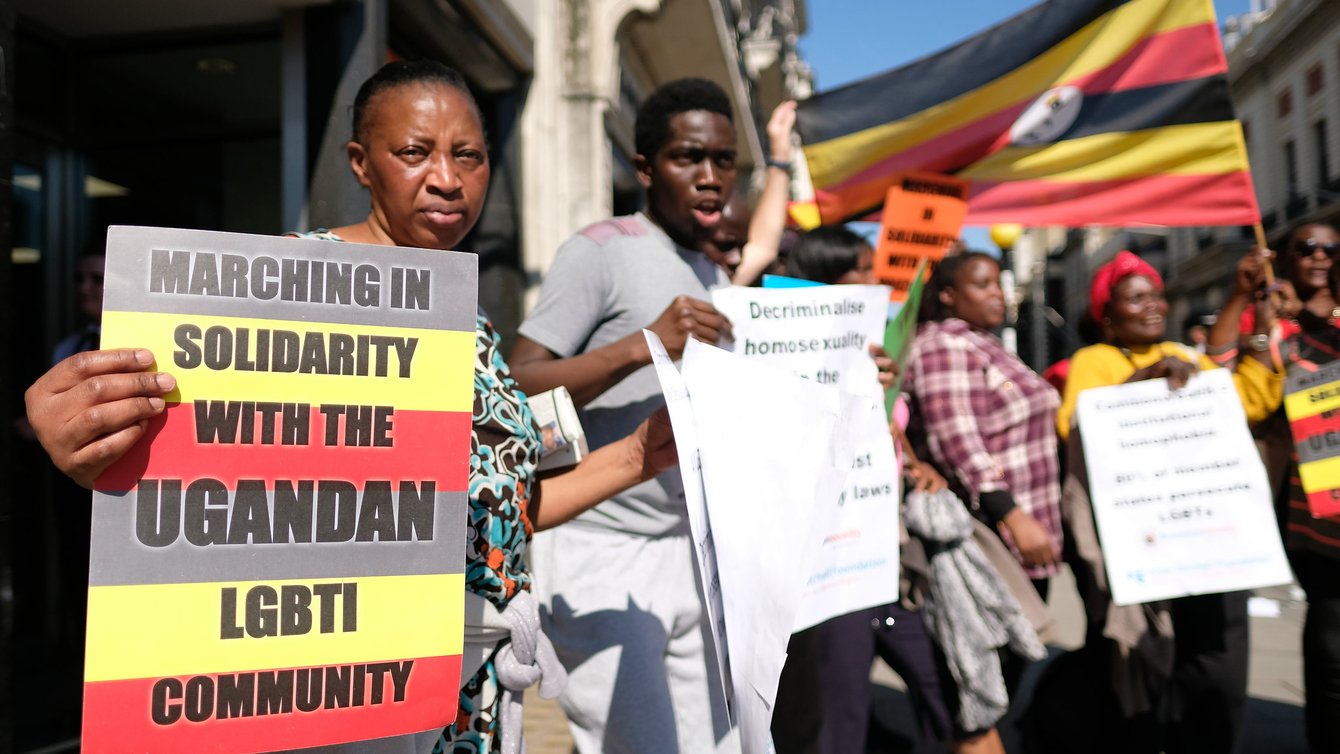 A woman in the front of the frame holding a sign that reads "marching in solidarity with the Ugandan LGBTI Community"