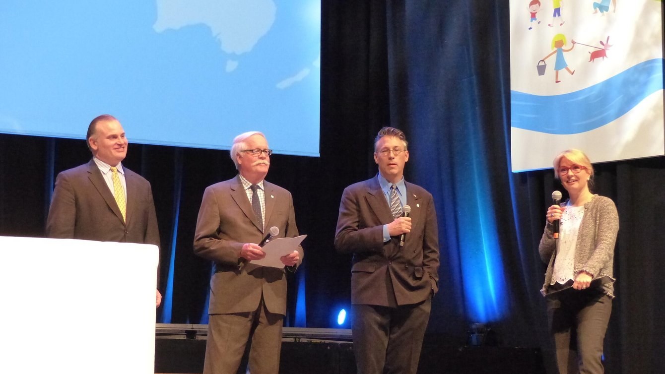 Three men in suits and a woman holding a mic.