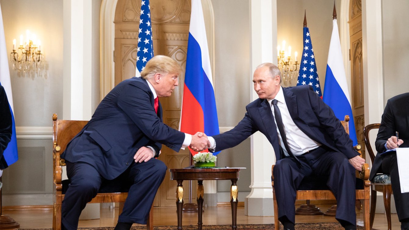 Two men in suits leaning over a table shaking hands
