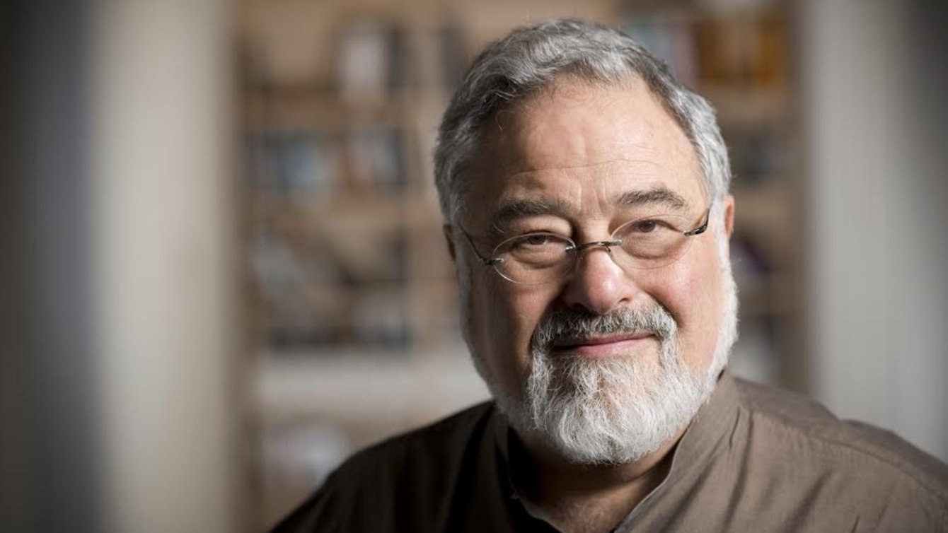A man with grey hair and grey beard wearing spectacles