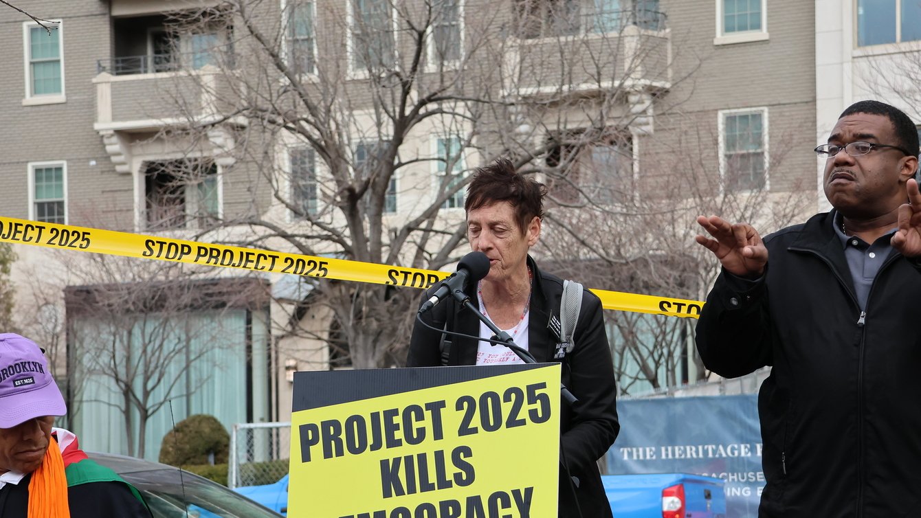 Two people on a podium with a board that reads "Project 2025 Kills Democracy"