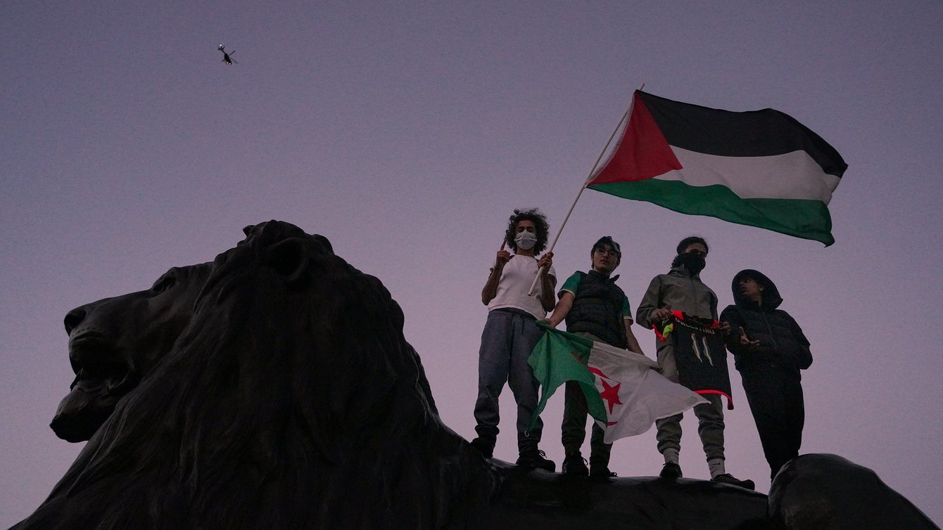 Four people carrying a Palestinian flag standing on a lion.