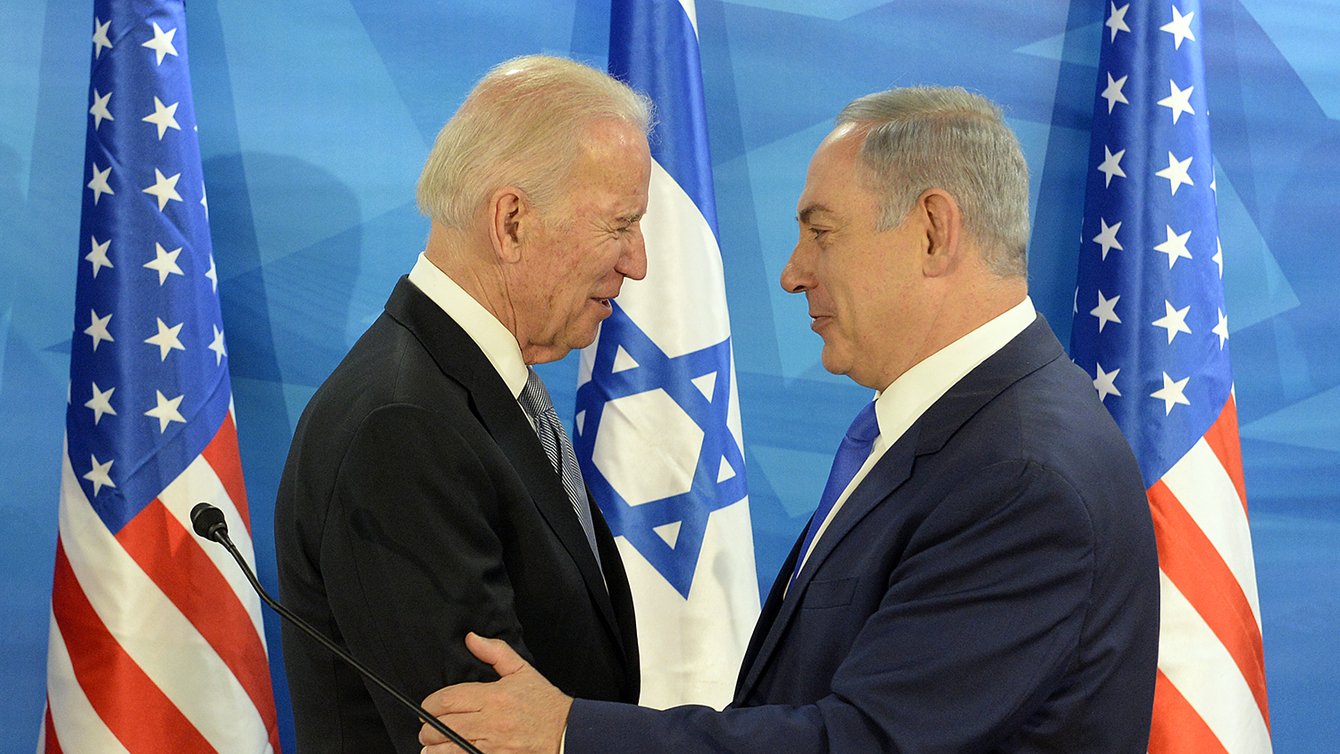 Two men in suits standing in front of the Israeli and US flags