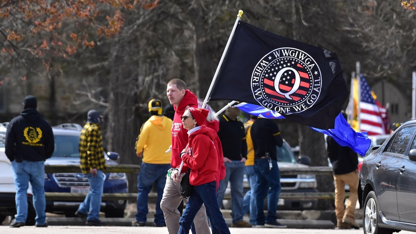 Two people in red hoodies carrying a QAnon flag