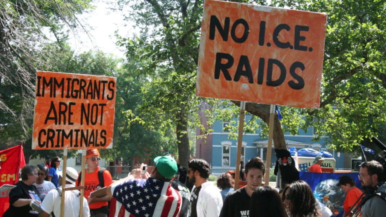 Protestors with signs saying "Immigrants are not criminals" and "No I.C.E. raids"