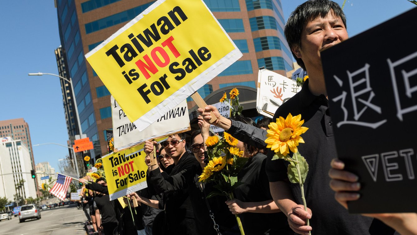people standing in a row holding sunflowers. A sign says "Taiwan is not for sale."