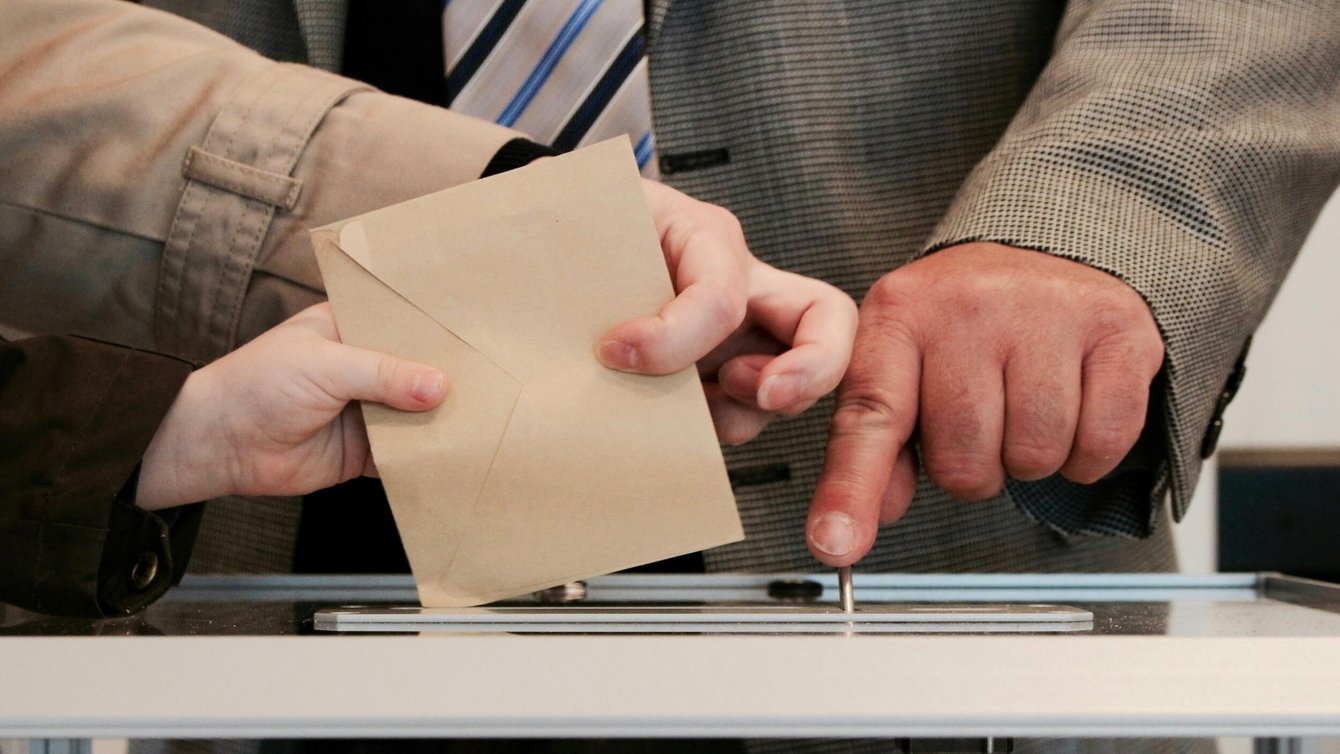a person dropping an envelope into a ballot box.