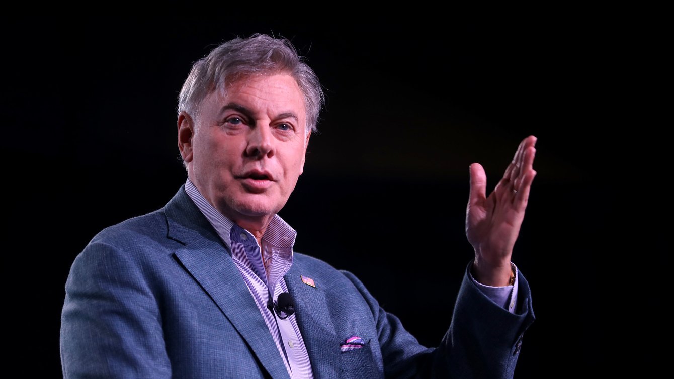 A man in a suit talking with his hand raised.