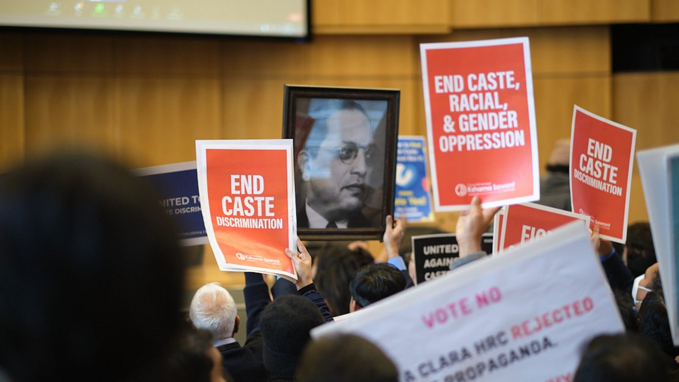 People holding banners that say "End Caste Discrimintaion" and "End Caste, Racial, And Gender Opression" and a picture of Dr. Ambedkar.
