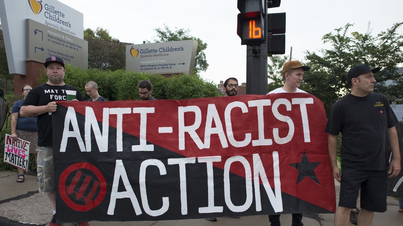 People holding a red and black flag that reads Anti-Racist Action