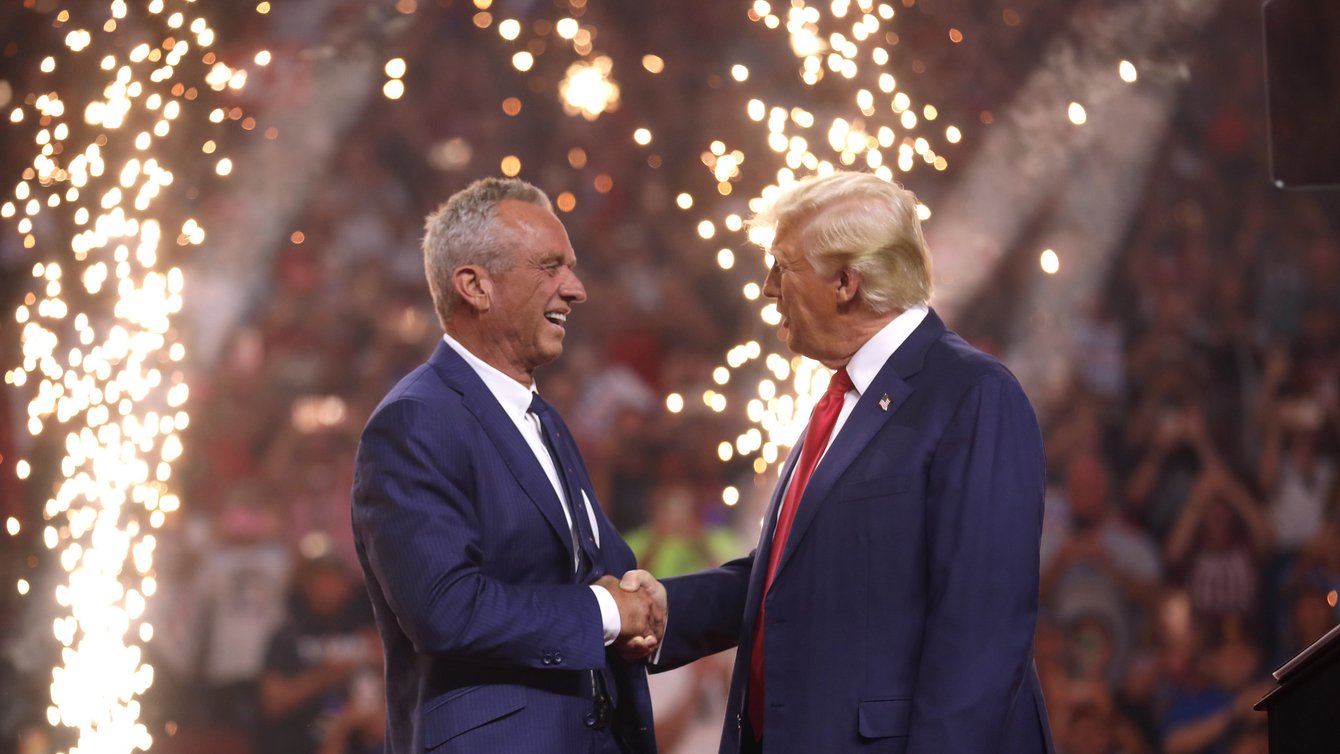 Two men shaking hands with fireworks behind them.