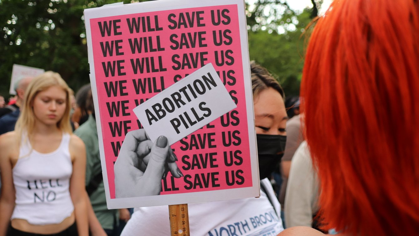a sign that reads "We will save us" over and over again with a hand that holds a paper that says "Abortion Pills"