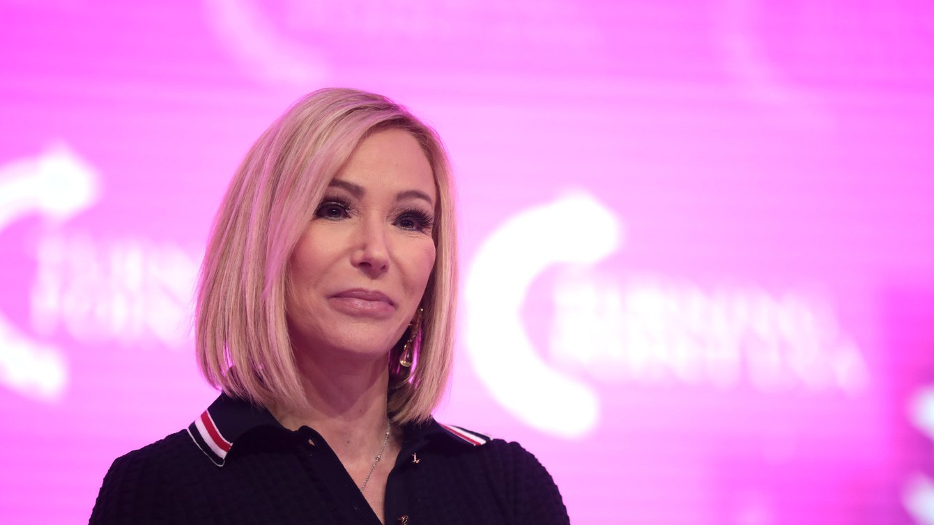 A woman in a black polo shirt with a pink background