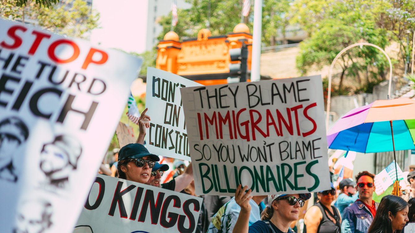 A protestor holding a sign saying "The blame immigrants so you won't blame billionaires"