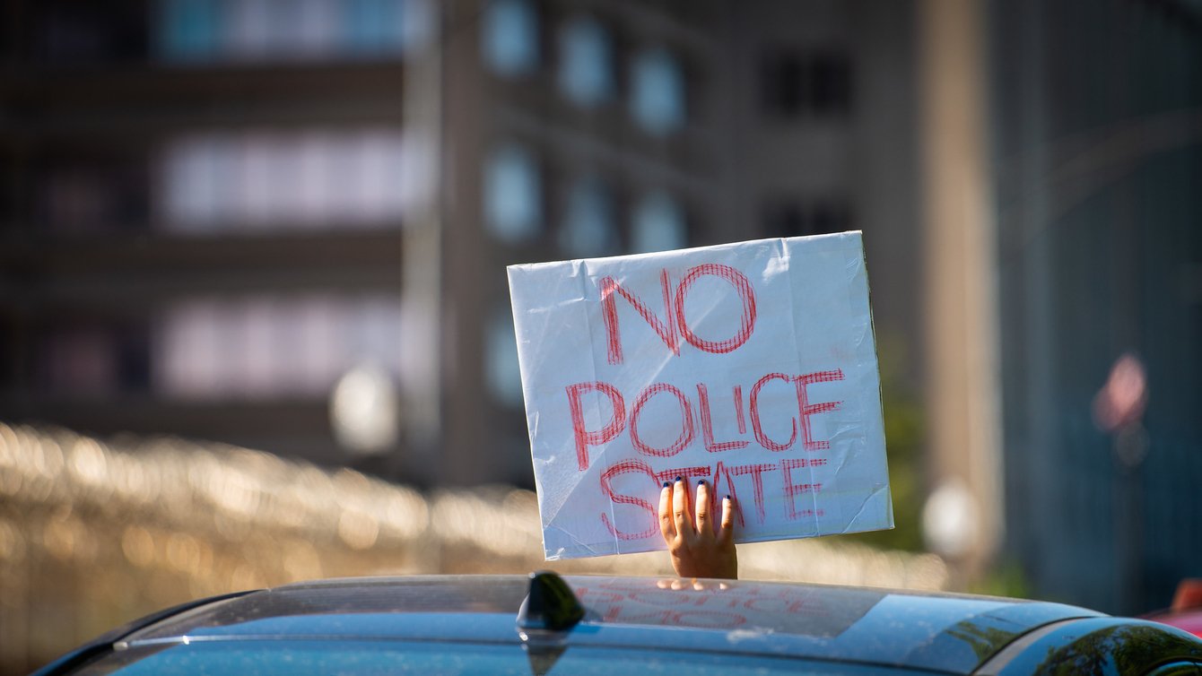 A person holding a sign out of a sun roof that reads "no police state"