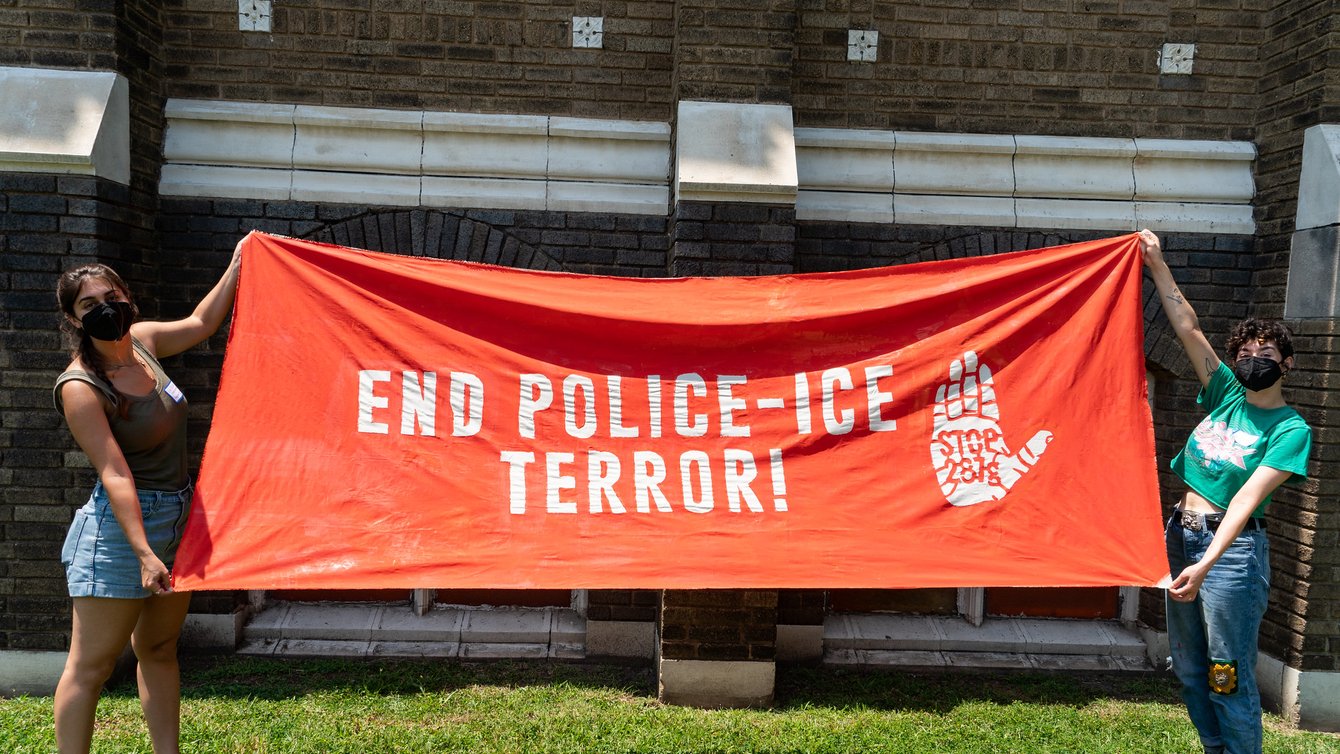 two people holding a banner that reads "End Police-ICE Terror" with a palm with 287g on it.