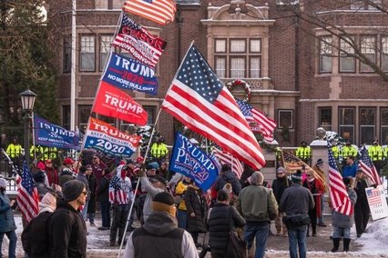A group of people gathered holding many Trump flags