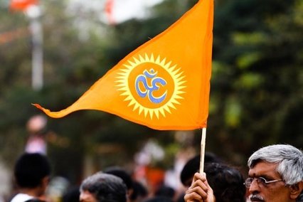 A man holding a saffron triangular flag with an "om" symbol on it.