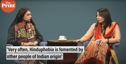 Two women sitting around a coffee table with a cup of coffee on it. The screen says "The Print" on the top left corner and the caption "very often, Hinduphobia is fomented by other people of Indian origin" is at the bottom of the screen.