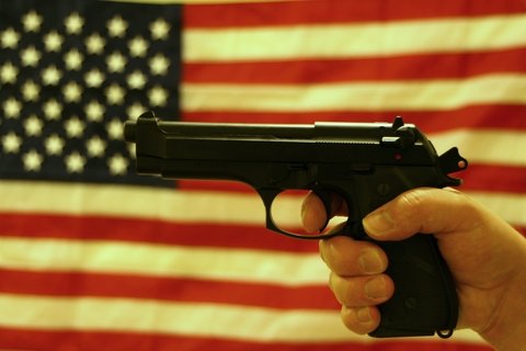 A hand gripping a handgun in front of an American flag backdrop