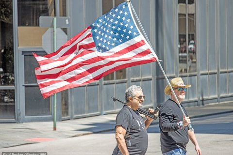 Coronavirus lockdown protestors hold American flag and gun, April 21, 2020 (Credit: Becker1999/flickr)