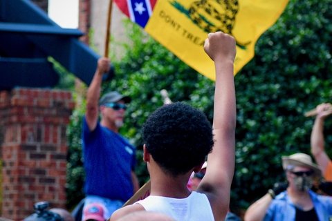 Pro-confederacy protestor holds up a confederate flag, a counter-protestor raises a fist in response. 